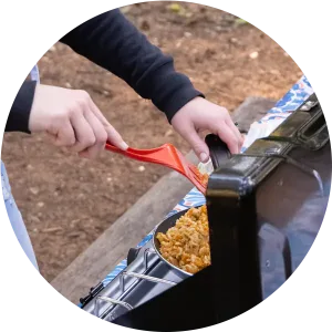 A close up of a woman cooking dinner on a camp stove with a red spatula.