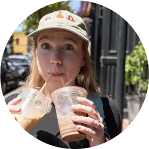 A woman is sipping on two coffees, one iced and one blended, with a happy look on her face.