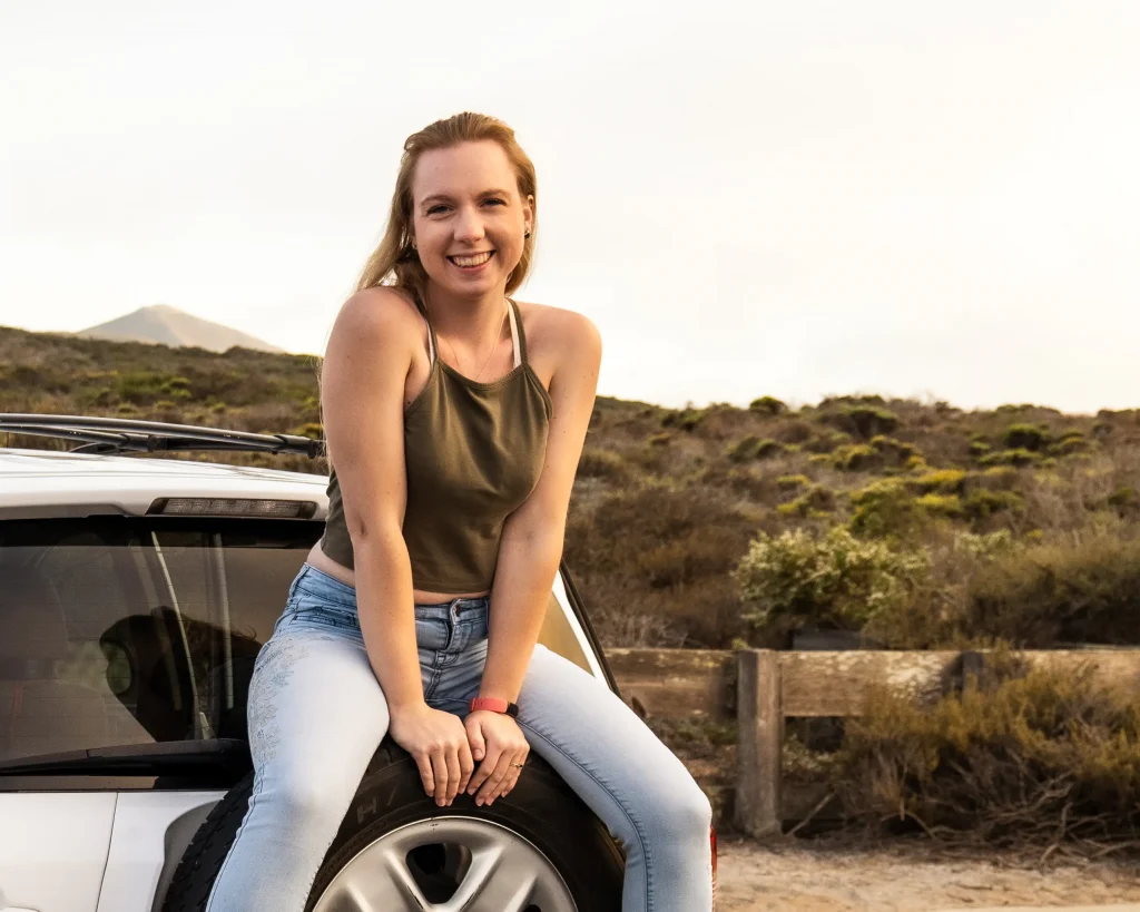 A close up of a woman sitting on the spare tire of a white Rav4.