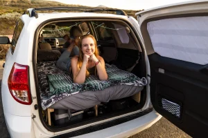 Looking into the back of a car where a woman is laying on the DIY camper bed set up.