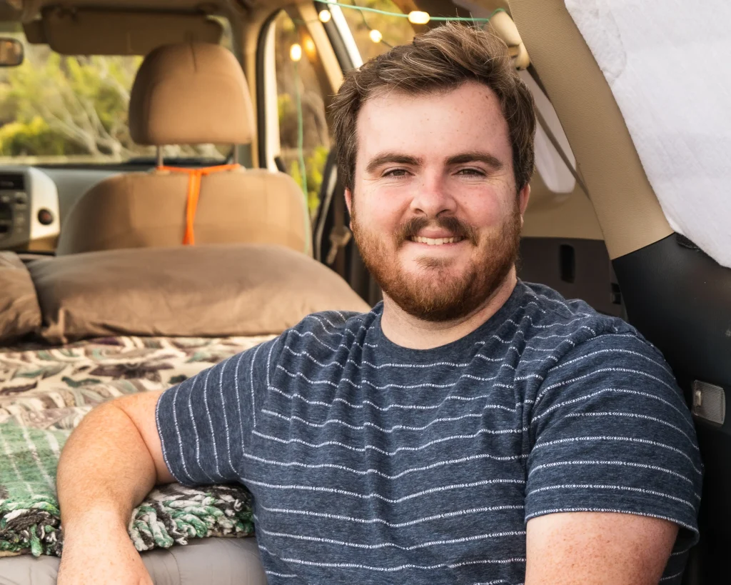 A man is looking at the camera while sitting in the back of the car camper.